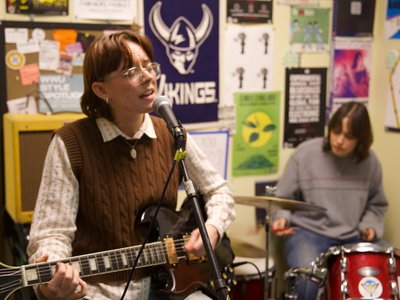 Two of the band sit and play their instruments with the Wavelength office in the background