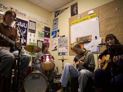 The full band sit in the Wavelength office playing their instruments