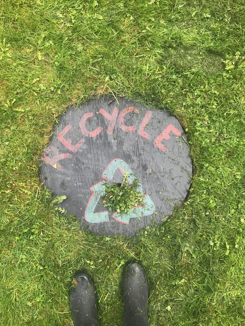 Two boots next to a handmade recycle sign in the grass