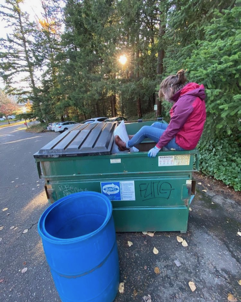 Kait sitting on the edge of a dumpster pulling out a bag of trash with her feet for a waste audit.