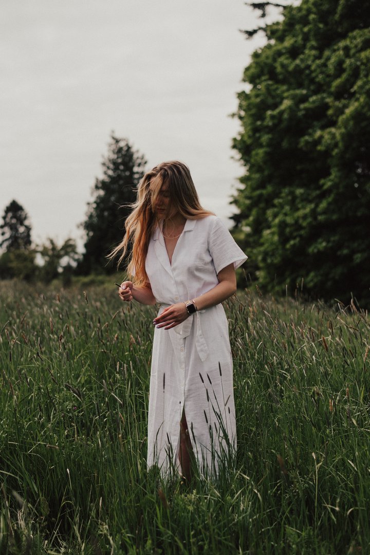 Photo of someone in a white dress with long blonde hair moving through a field of tall grass