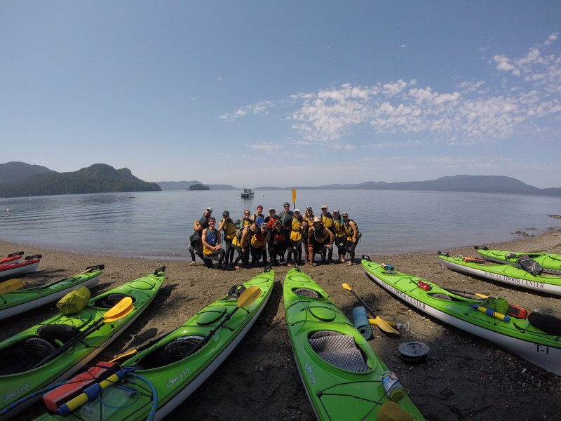 Beach view with green kayaks in the foreground and students in the back