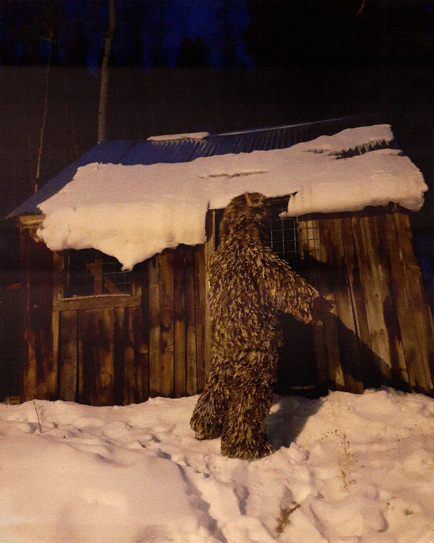 Image of figure wearing artwork in front of a shed standing in snow at night 1.png